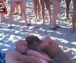 Um trio de sexo de uma mulher e dois homens está em pleno andamento em uma praia. mas marrom algumas pessoas não será. um círculo de voyeurs é olhar e tirar e levar os filhos da puta todo o sol.